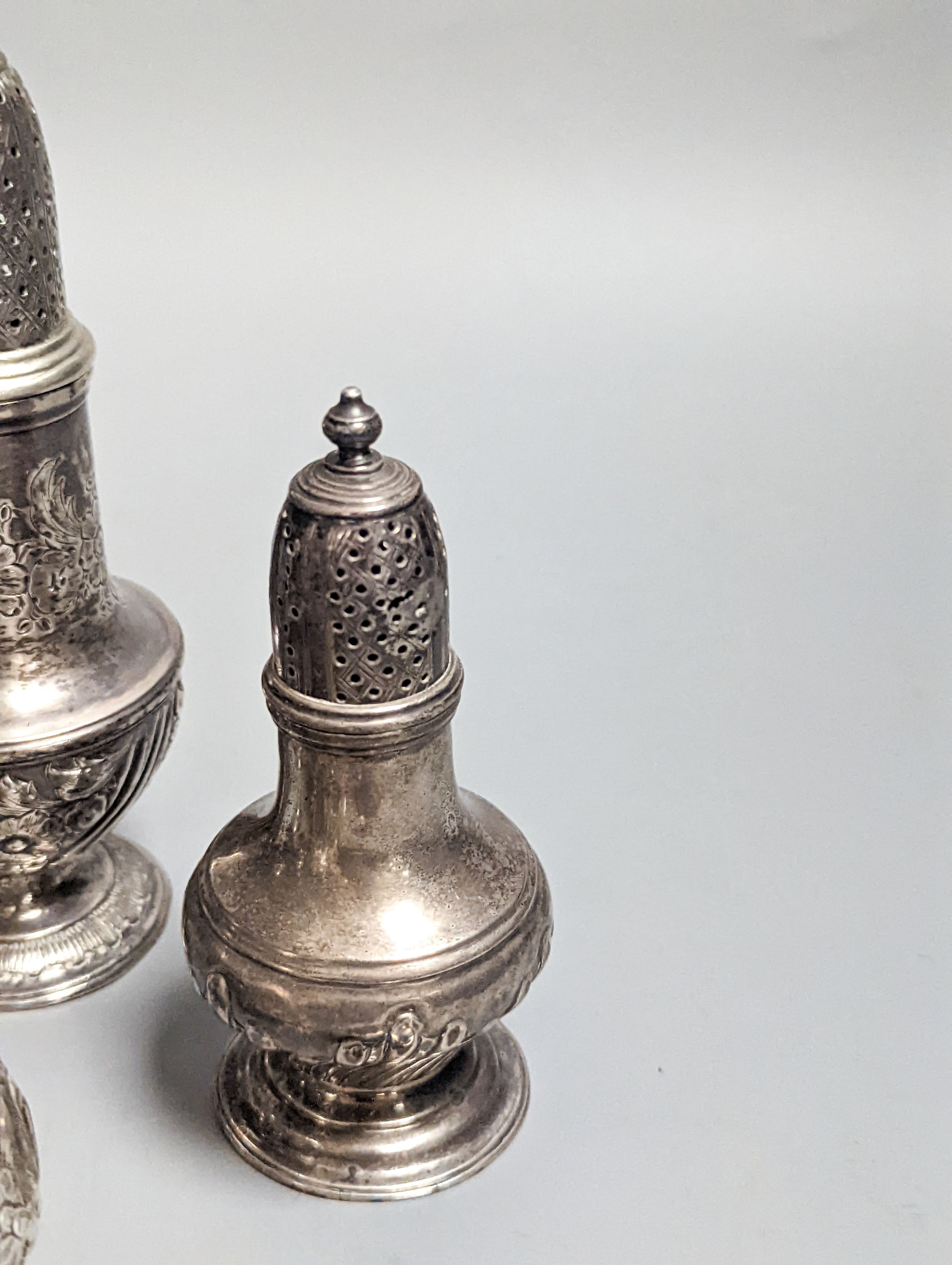 A Victorian embossed silver cream jug, London, 1883, 92mm, two 18th century silver pepperettes, one with plated cover, four later condiments (two silver), a silver spoon and small 800 standard photograph frame.